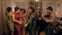 Actors in a living room set dressed in 60s clothing, dancing
