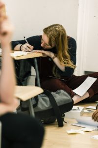 Student sat on floor writing at a chair