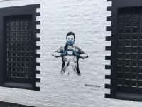 Photo of white wall with grafitti of a doctor wearing a mask and gloves making a heart shape with her hands