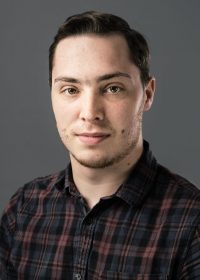 headshot of white male student with dark brown hair in a plaid shirt looking at camera