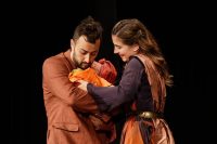 Two actors on stage in robes, holding a baby between them