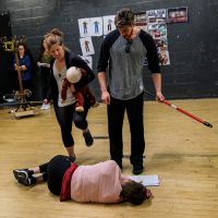 Two students kicking another student who is on the ground in rehearsal