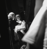 Black and white photo of female being dressed by dresser, reflection in mirror