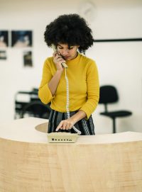 Acting student in rehearsal, stood behind a desk, speaking on a phone