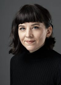 headshot of woman with short black hair and a full fringe in a black top