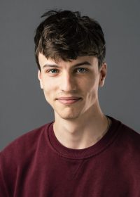 Headshot of male white student with dark brown hair looking at camera, in a red jumper