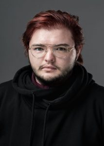 headshot of male student with red hair and glasses looking at camera, wearing a black hoody