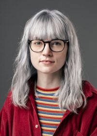 Headshot of woman in a red shirt with a stripey top, grey hair and glasses