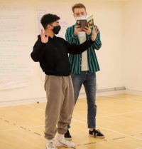 Two actors in rehearsal, one with arms outstretched, the other reading from Hedda