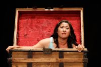 Actor sat in large wooden trunk with lid open, red lining
