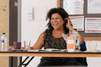 Director Nancy Medina sat at a table watching rehearsals and smiling