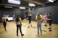 Acting students are grouped around a central tutor in a studio playing a game