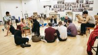 Photo of a group of students talking to a director in the rehearsal room with students sat in a circle on the floor